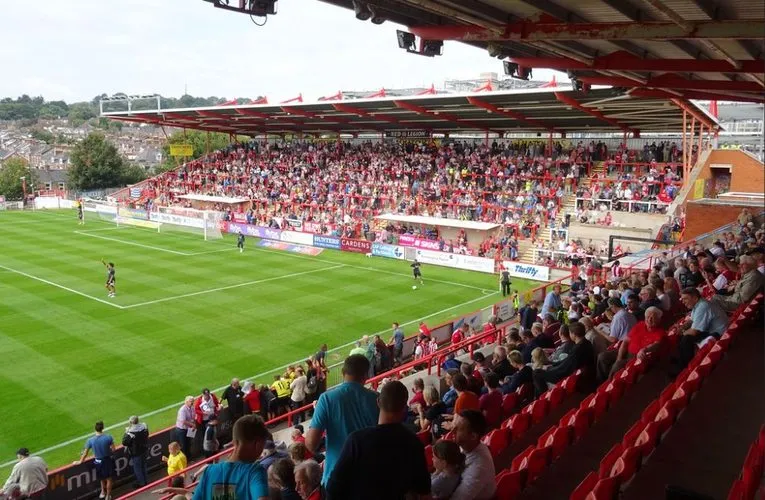 Bầu không khí sôi động trên khán đài sân St. James Park của Exeter City vào ngày diễn ra trận đấu, với các cổ động viên đang cổ vũ nhiệt tình.