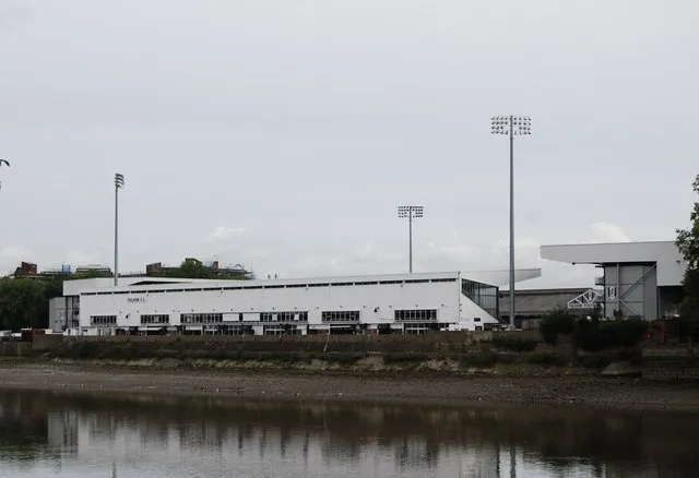 Góc nhìn toàn cảnh sân vận động Craven Cottage từ sông Thames, nổi bật với kiến trúc truyền thống và vẻ đẹp ven sông.