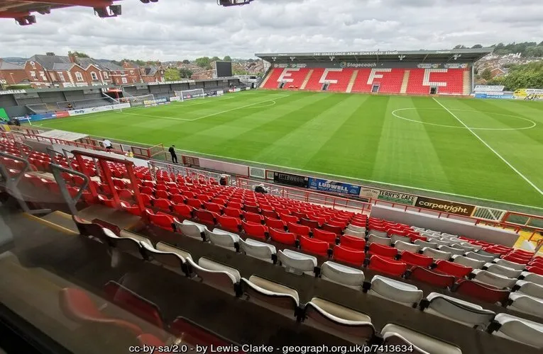 Góc nhìn tổng thể mặt sân cỏ xanh mướt và khán đài từ bên trong sân vận động St. James Park, Exeter, sẵn sàng cho trận đấu.