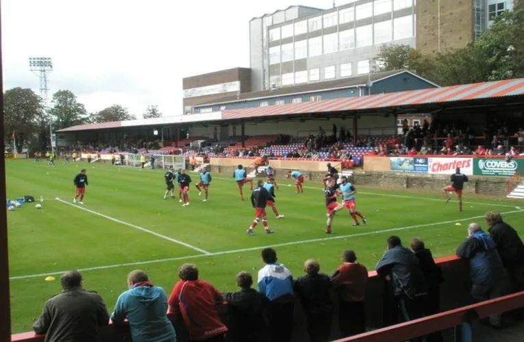 Góc nhìn từ khán đài bên trong sân Recreation Ground Aldershot Town, bao quát toàn bộ mặt sân và các khu vực chỗ ngồi