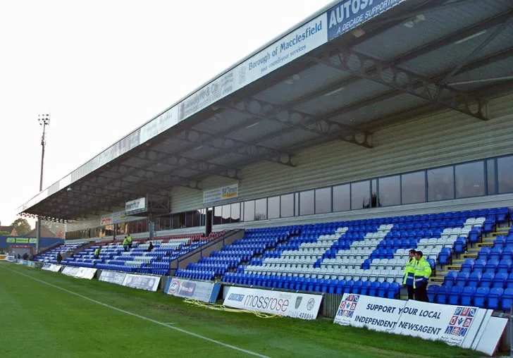 Khán đài chính với hàng ghế màu xanh đặc trưng của sân Moss Rose, nơi người hâm mộ Macclesfield Town theo dõi các trận đấu