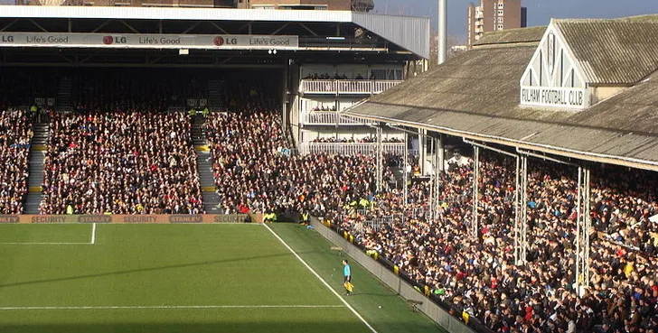 Toàn cảnh sân vận động Craven Cottage nhìn từ khán đài, cho thấy mặt cỏ xanh mướt và không khí trận đấu bóng đá.