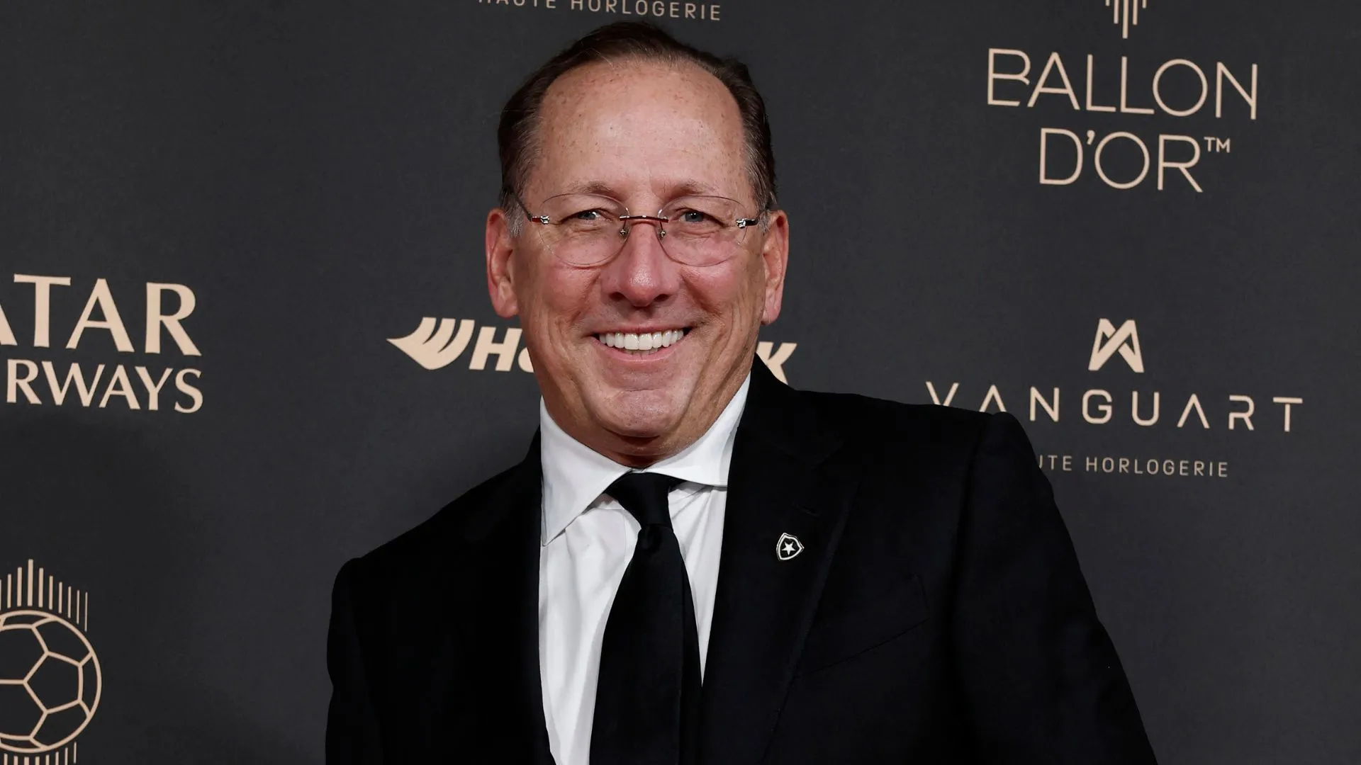 John Textor đứng ở sân bóng, góc nhìn cắt ngang với logo Eagle Football Group